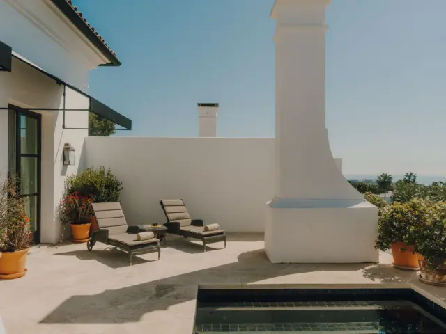 Piscina privada en terraza exterior de suite con vistas al mar, rodeada de paredes blancas, dos tumbonas, macetas