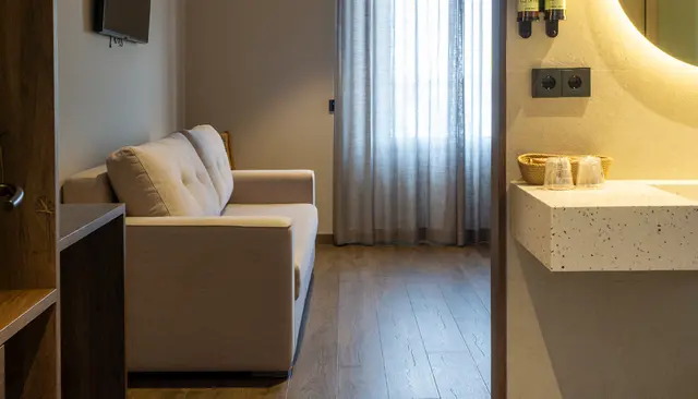 Vista parcial de un baño con encimera de lavabo de material terroso, grifo, espejo circular iluminado y accesorios.