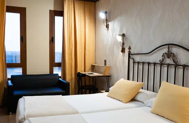 Vista de una habitación con una cama de matrimonio con cabecero de forja negra y almohadas amarillas, un sillón negro