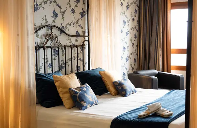 Vista de una suite con cama de matrimonio grande con cabecero de forja negra, múltiples cojines azules y amarillos