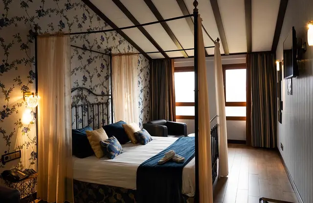 Habitación de suite con cama de matrimonio de cuatro postes con dosel, sábanas blancas, cojines azules y amarillos