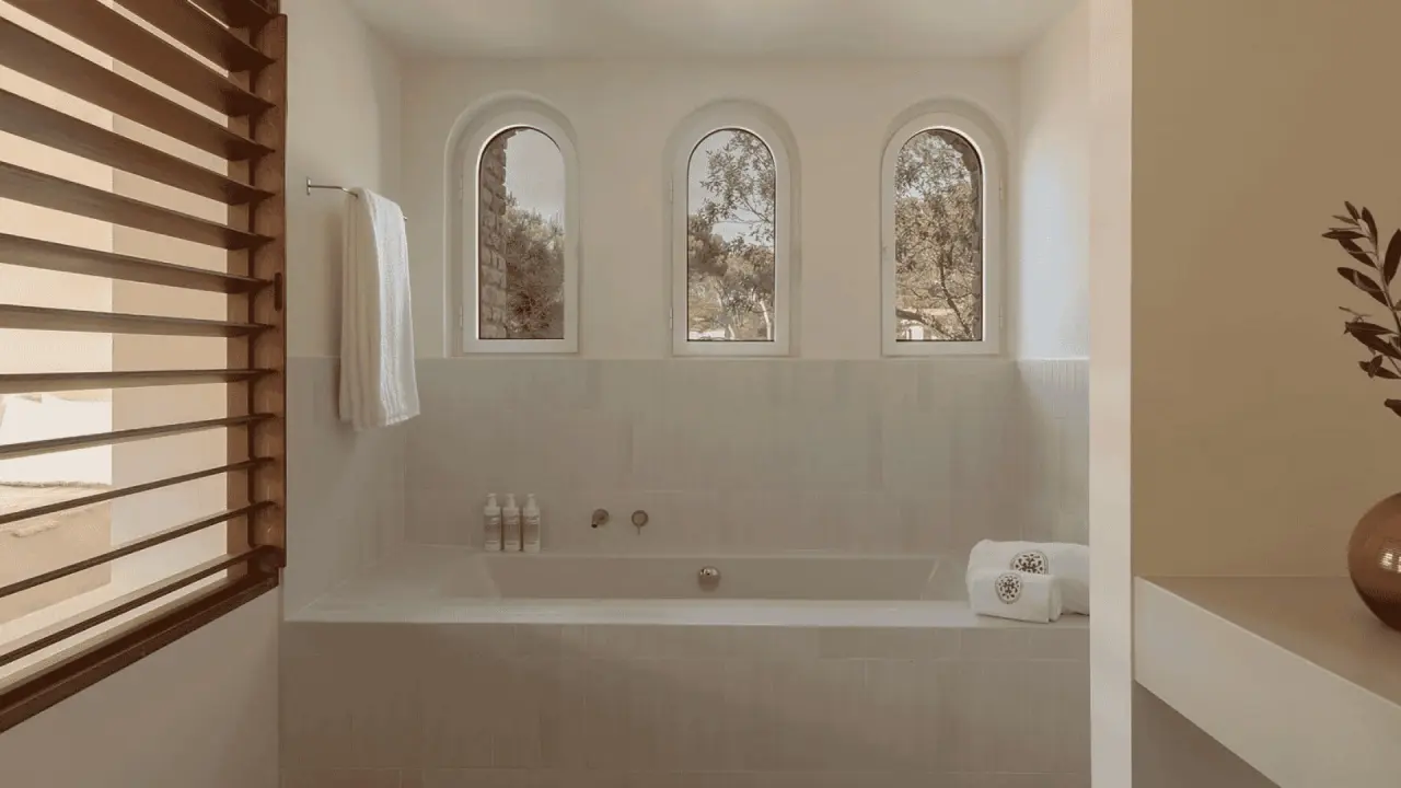 Baño con bañera empotrada, tres ventanas arqueadas y toallas blancas en un entorno minimalista.