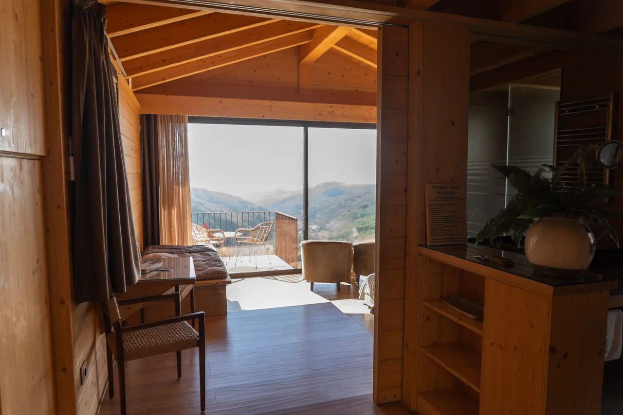 Interior de una suite tipo cabaña con paredes y techo de madera, suelo de tarima, zona de estar con sofá y sillones