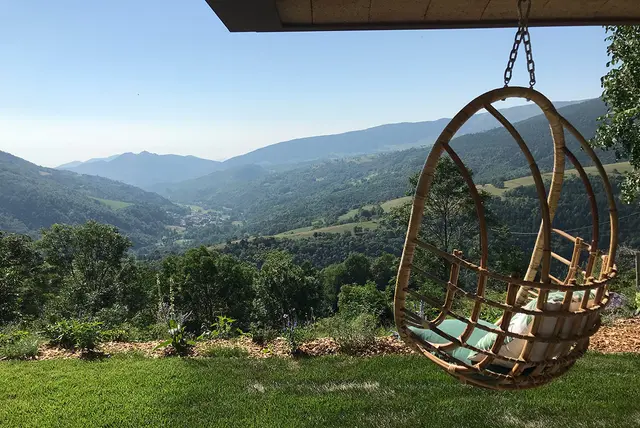 Vista panorámica de un valle montañoso con colinas verdes y un pueblo al fondo, tomada desde una terraza con un sillón