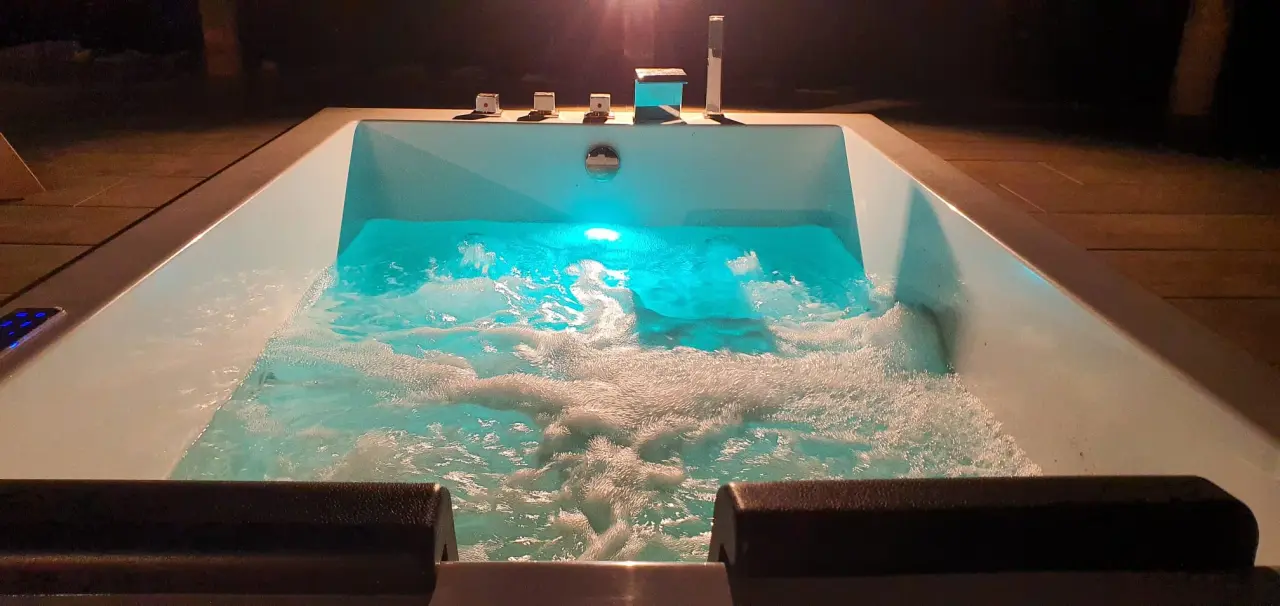 Jacuzzi exterior rectangular iluminado con agua burbujeante en terraza nocturna.
