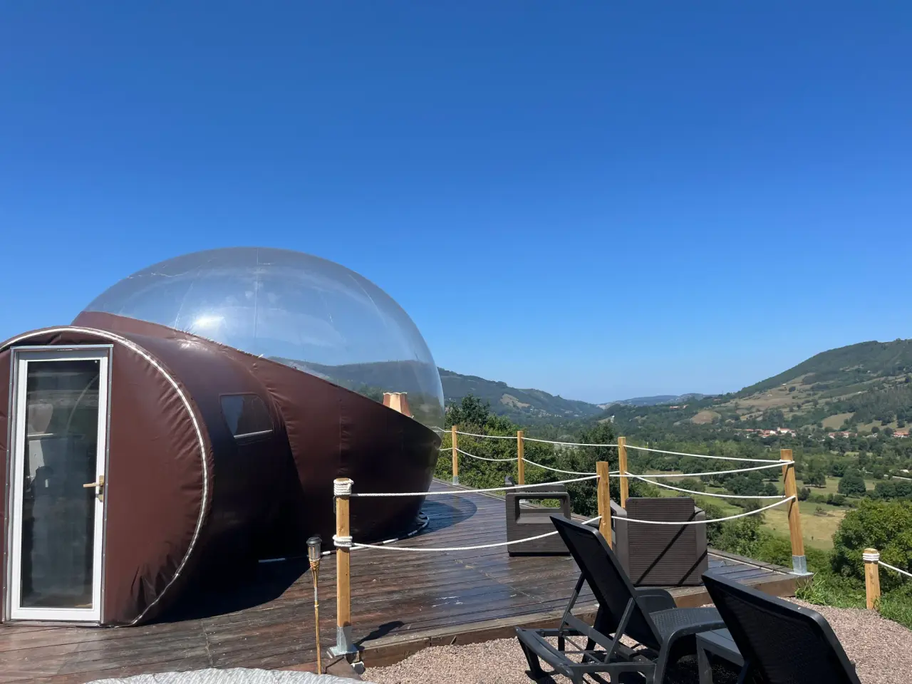 Vista exterior de una cabaña glamping con estructura semicircular y cúpula transparente, situada en una terraza