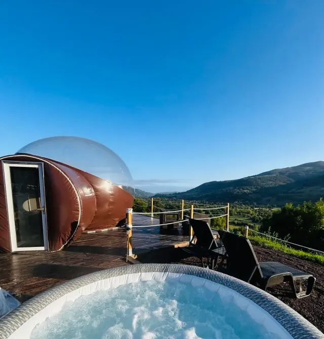 Jacuzzi hinchable en terraza de madera con vistas a las montañas y valles.