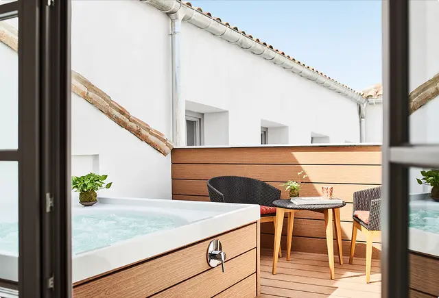 Jacuzzi rectangular empotrado en terraza privada con agua en movimiento, rodeado de tarima de madera, mesa redonda