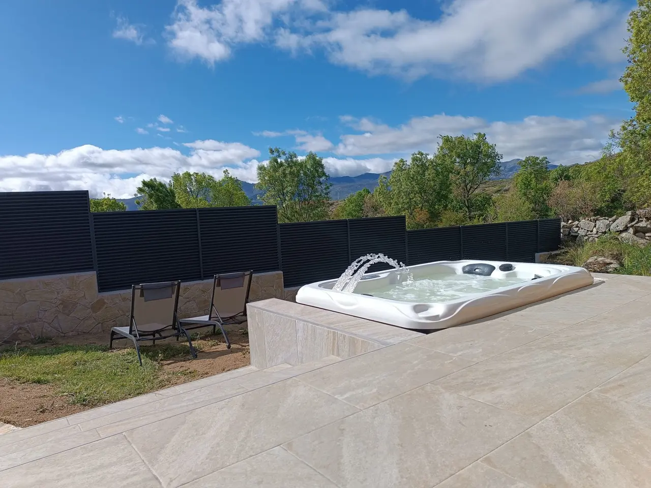 Bañera de hidromasaje exterior climatizada con chorros de agua en una terraza de piedra con vistas a las montañas.