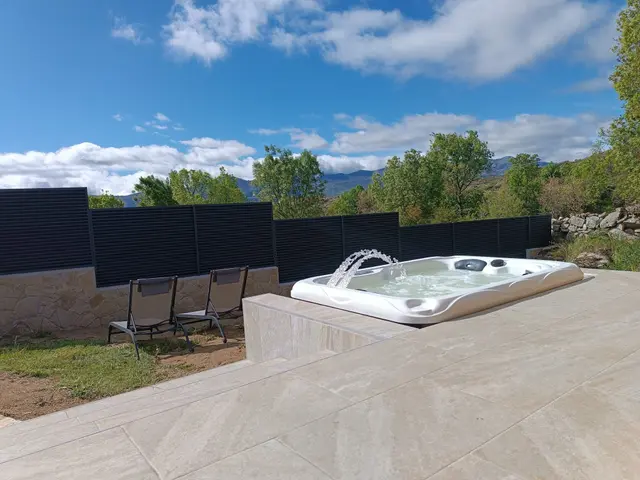 Bañera de hidromasaje exterior climatizada con chorros de agua en una terraza de piedra con vistas a las montañas.