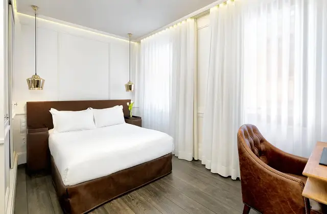 Habitación con cama doble grande vestida de blanco, cabecero marrón, dos mesitas de noche, dos lámparas colgantes