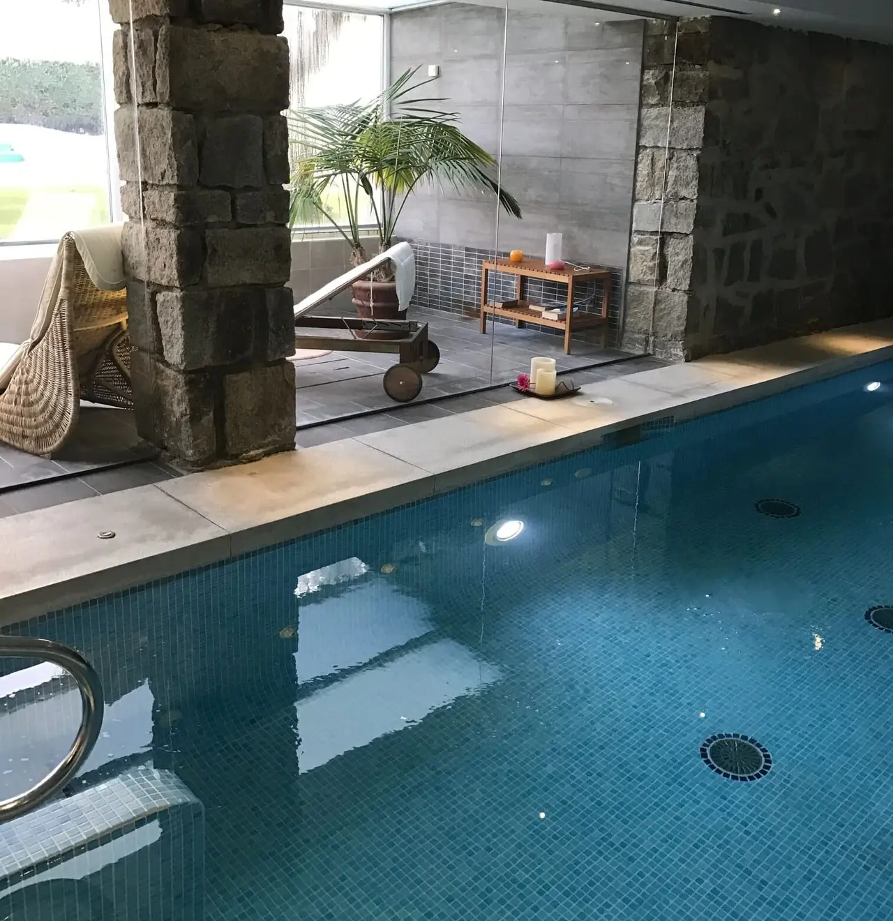 Interior de un spa privado con piscina rectangular de agua azul iluminada desde el fondo, rodeada de bordes de piedra