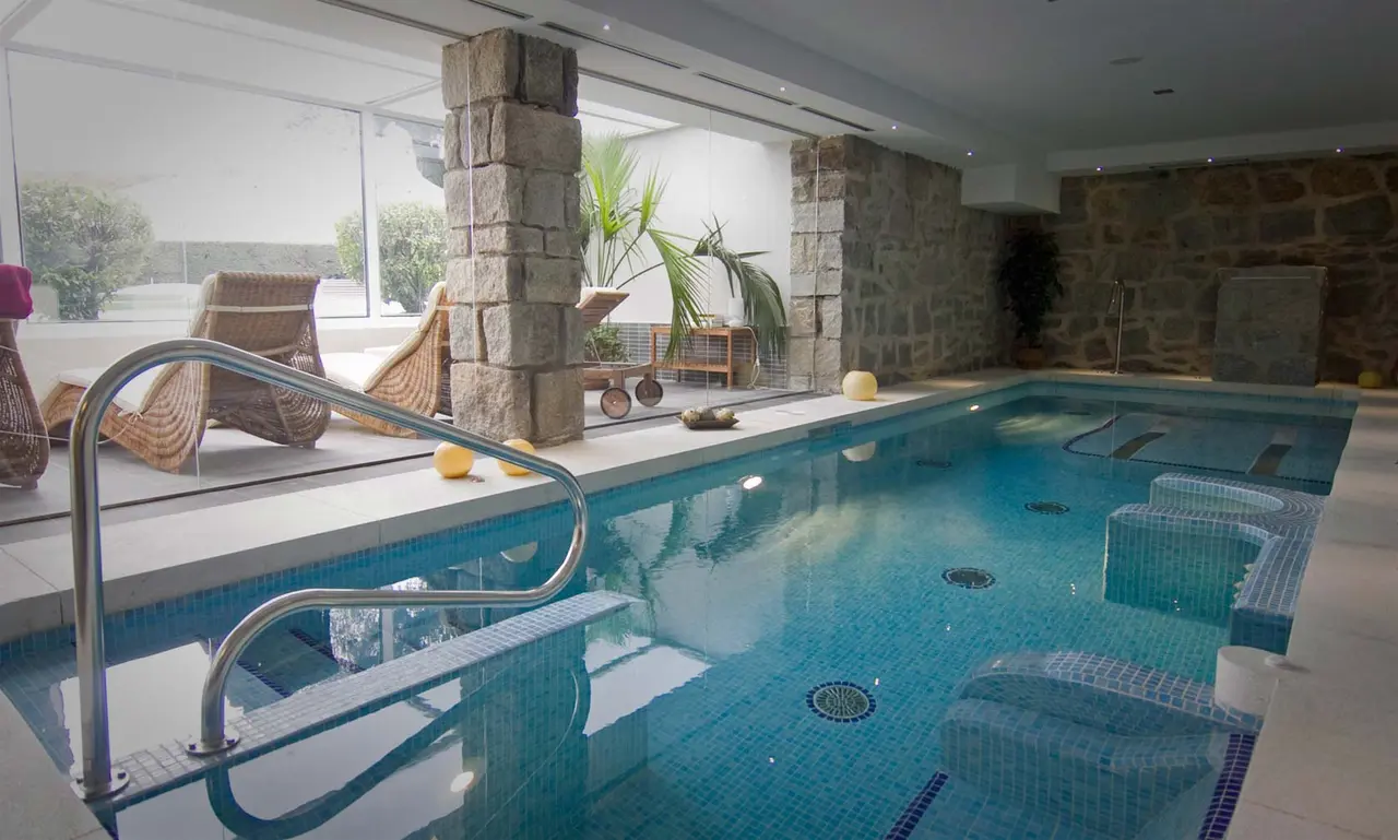 Interior de un spa privado con piscina de agua azul de mosaico, asientos sumergidos, barandilla metálica de acceso