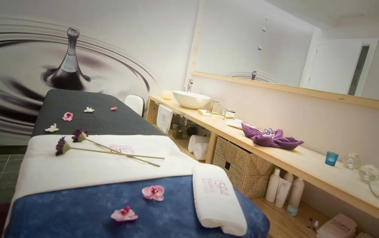 Vista de un spa privado con camilla de masaje cubierta por toallas blancas y azules, decorada con pétalos de flores