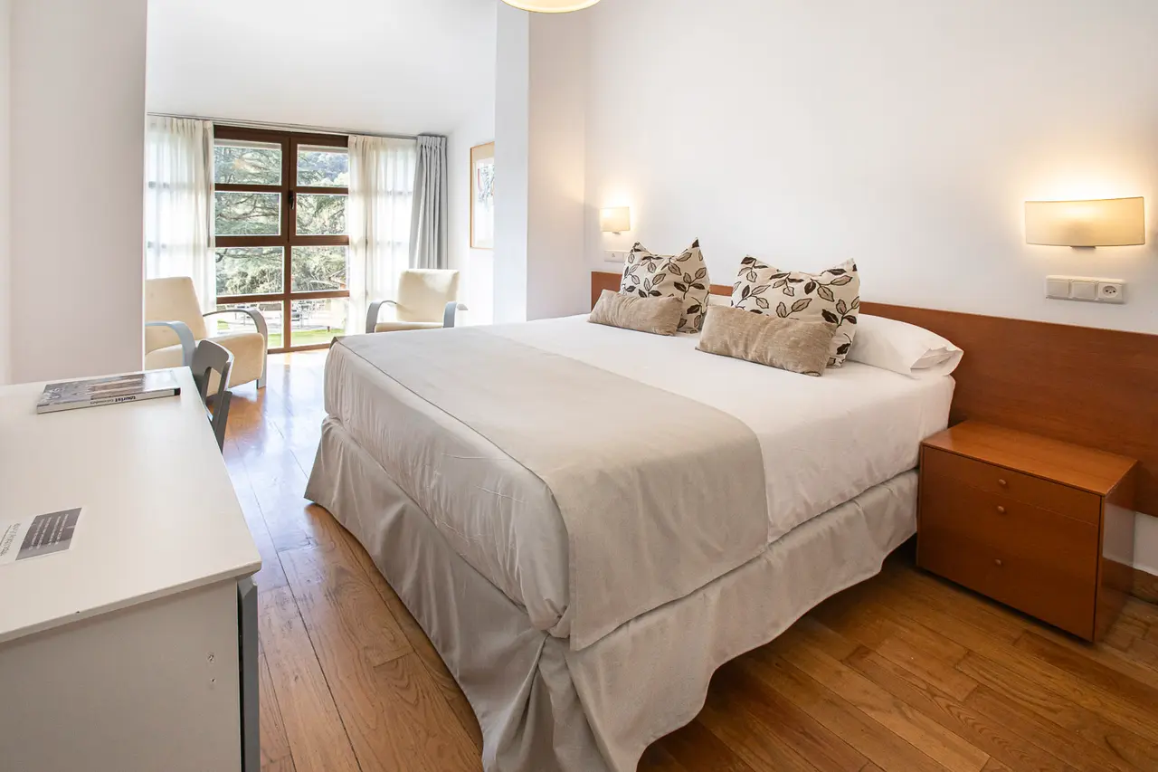 Habitación doble con cama grande, escritorio, sillones y ventana al exterior.