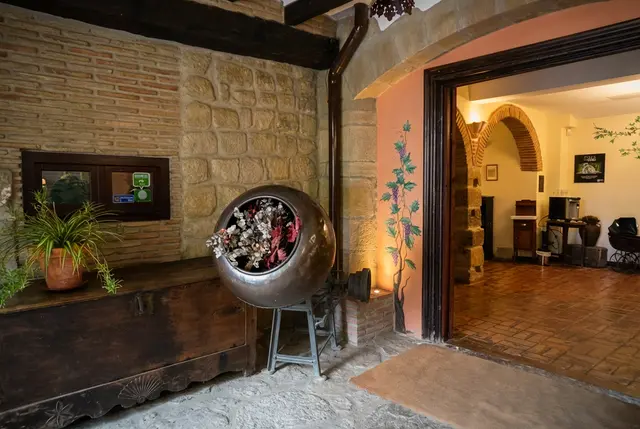 Entrada a una suite con paredes de piedra y ladrillo, suelo de terrazo, un gran macetero metálico con flores secas