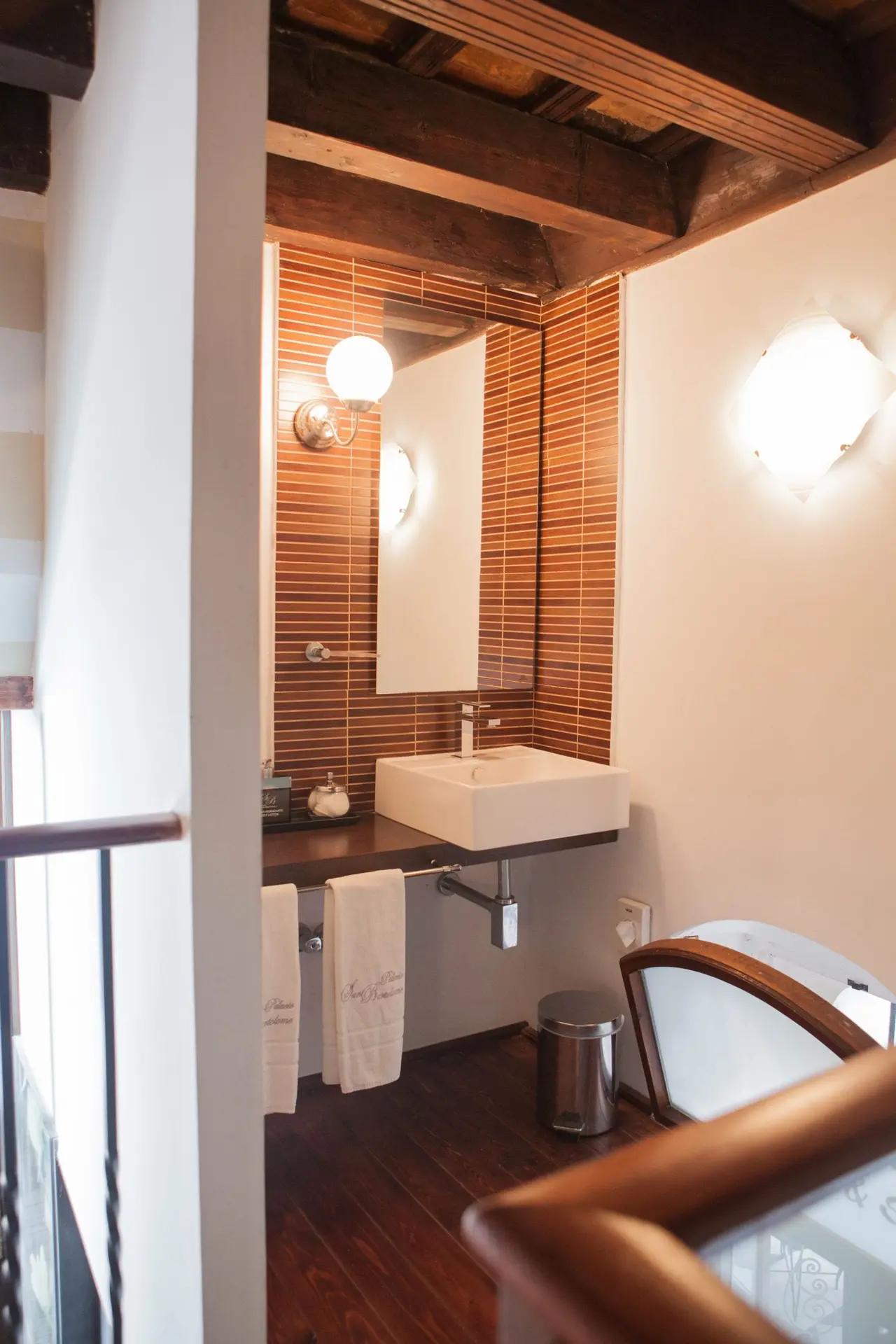 Vista de un baño con lavabo cuadrado blanco sobre encimera de madera oscura, espejo rectangular, grifería cromada