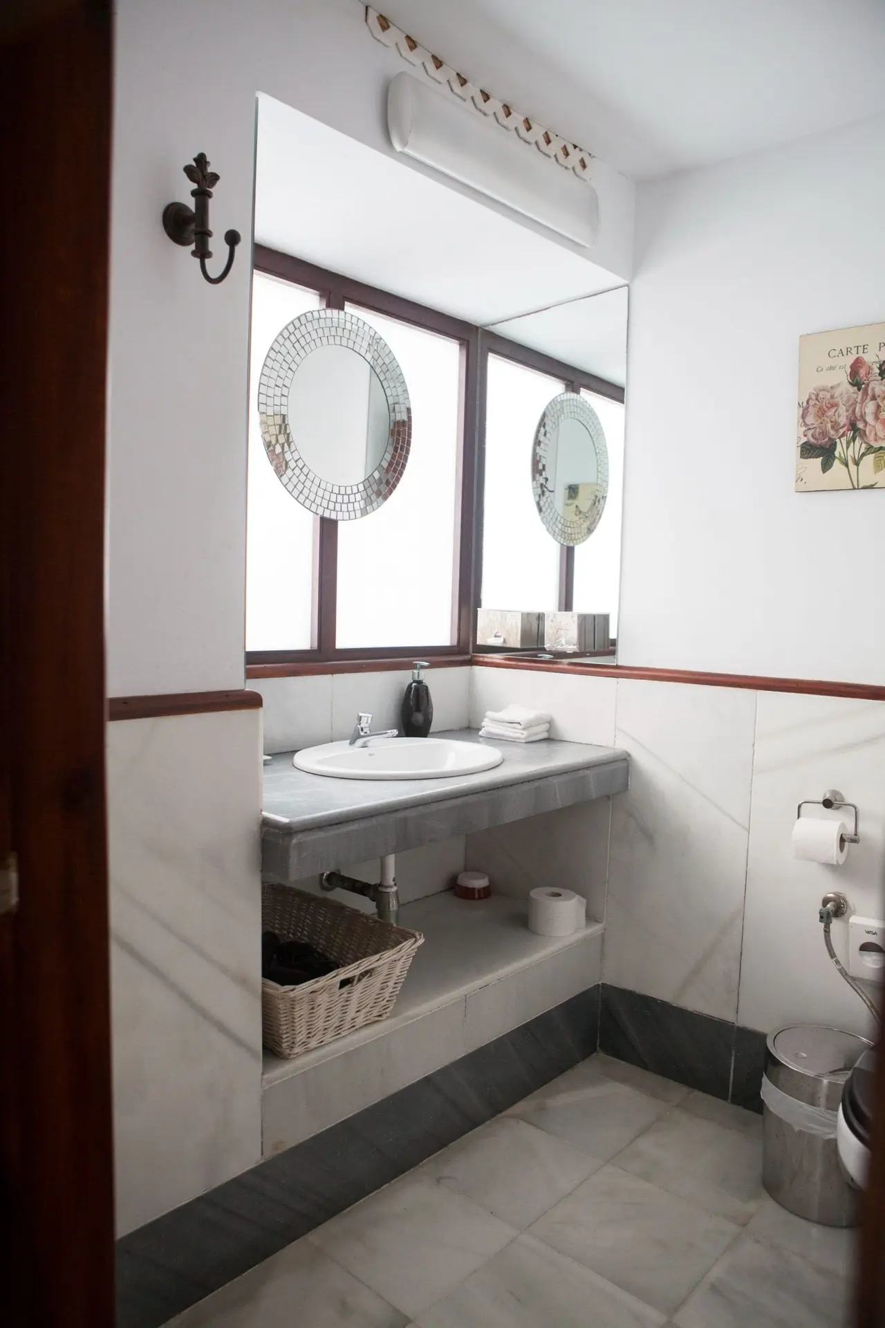 Baño con lavabo redondo blanco sobre encimera de mármol gris, grifo cromado, espejo circular de mosaico, toallas