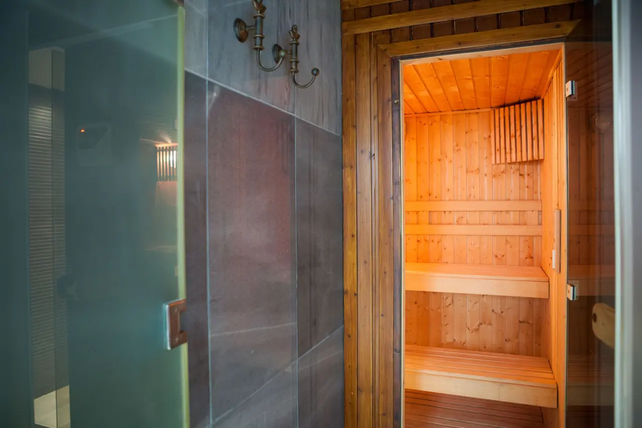 Vista de un spa privado con una sauna de madera iluminada y una ducha de vidrio adyacente con paredes de piedra oscura.