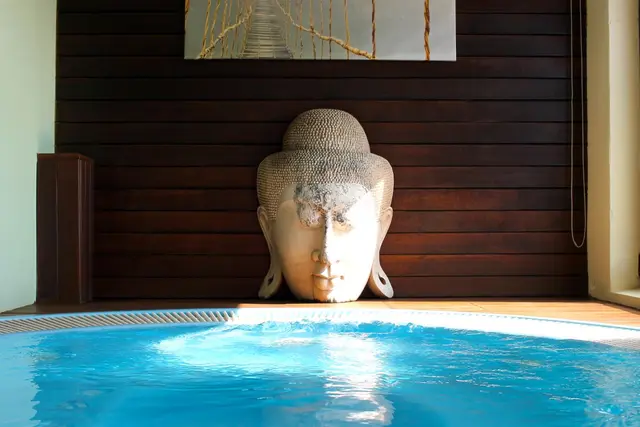 Jacuzzi circular con agua azul en una terraza privada, frente a una pared de madera oscura con una gran escultura