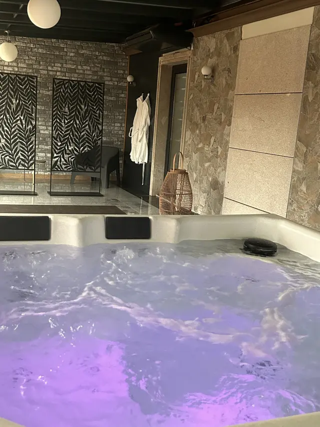 Vista de un spa privado con jacuzzi iluminado en tonos morados, rodeado de paredes de piedra y ladrillo visto