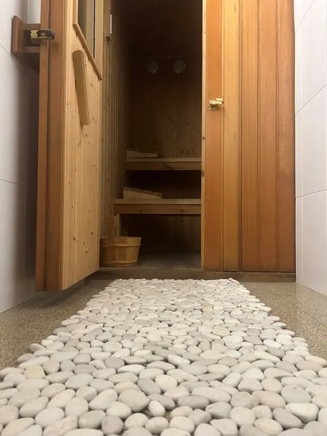 Entrada a un spa privado con sauna de madera, bancos escalonados, cubo de madera y camino de piedras blancas
