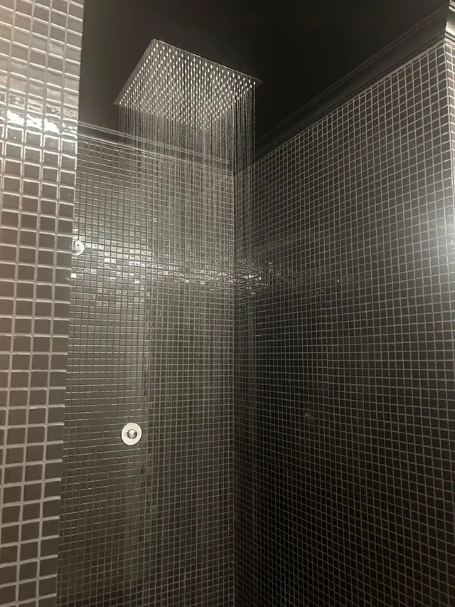 Ducha de efecto lluvia en un spa privado con paredes de mosaico negro y un cabezal de ducha cuadrado grande que libera