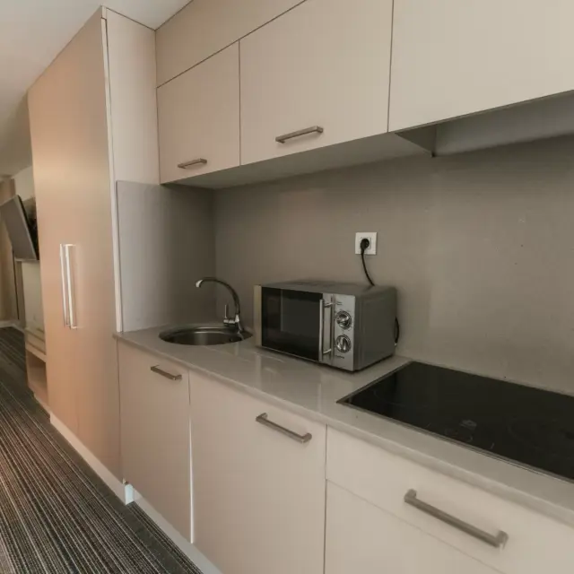 Cocina compacta con encimera blanca, armarios superiores e inferiores en tono beige, fregadero de acero inoxidable