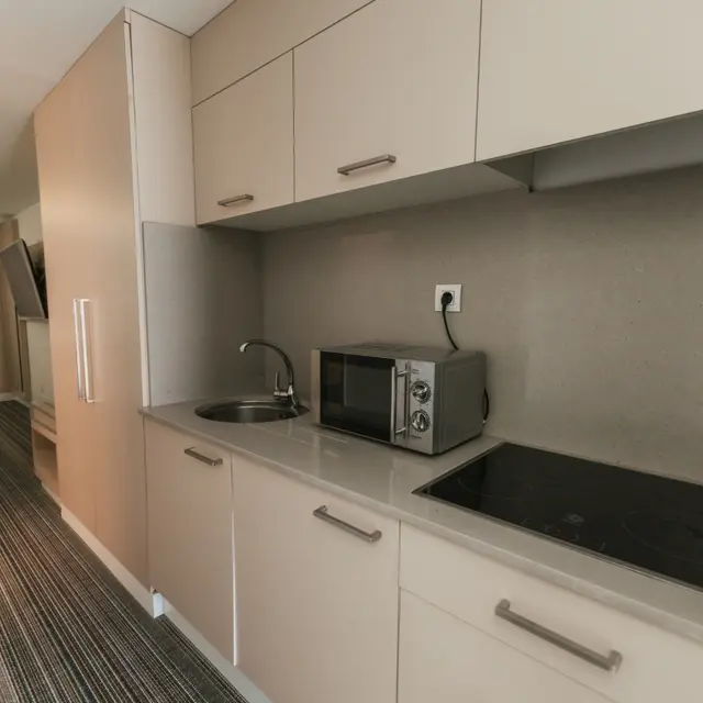 Cocina pequeña con armarios beige, encimera de piedra clara, fregadero con grifo, microondas y placa de inducción.