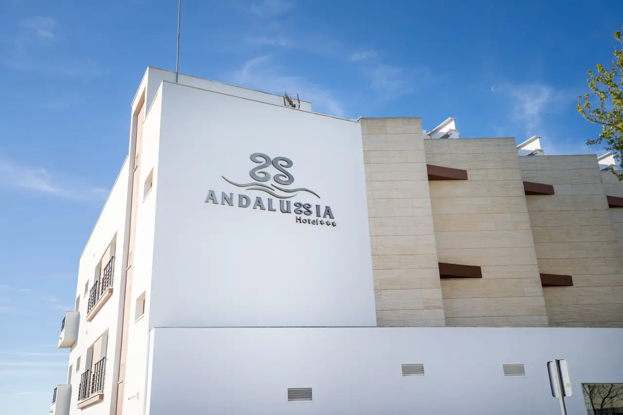 Fachada exterior del edificio del Hotel Andalussia con su logo en relieve sobre una pared blanca, bajo un cielo azul