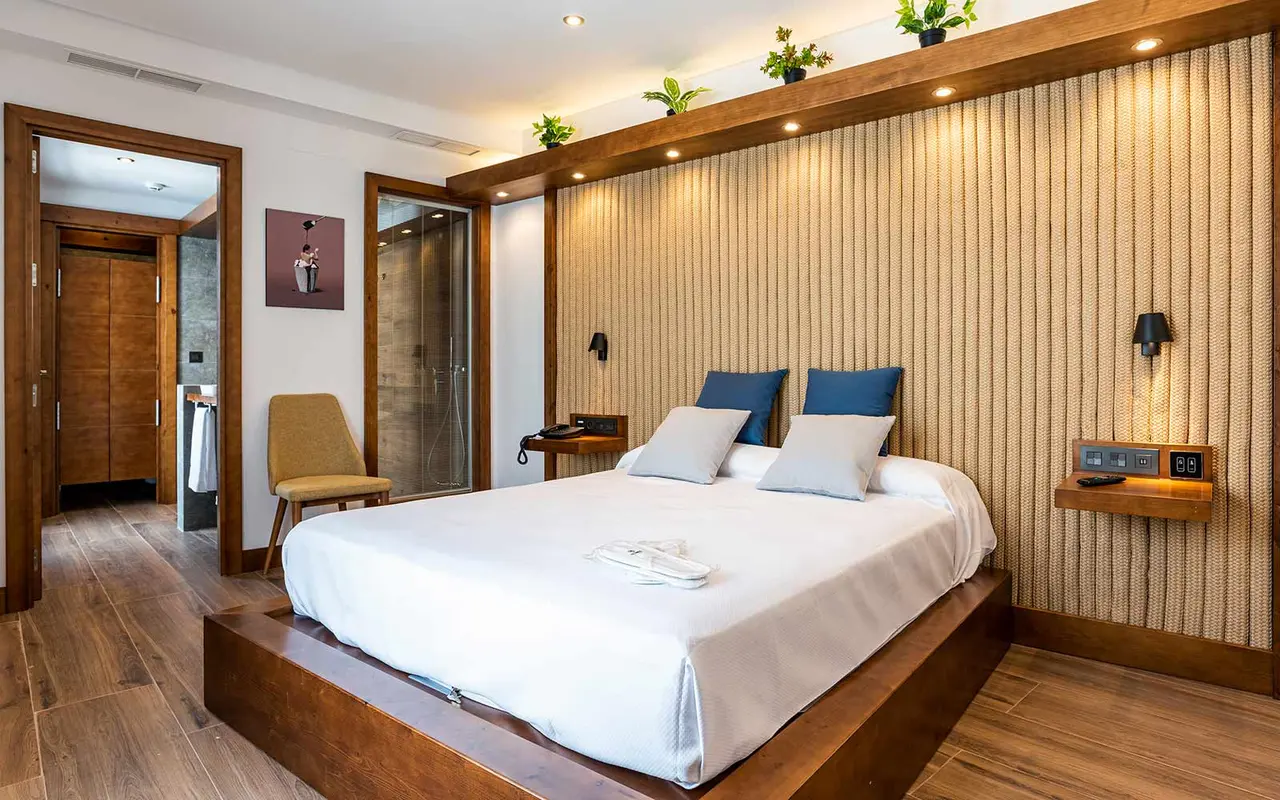 Vista de una habitación junior suite con cama king size sobre base de madera, cabecero alto de madera con listones