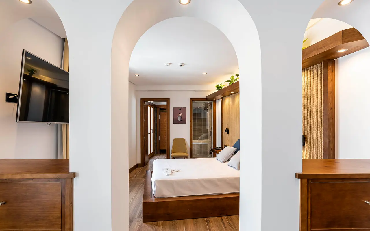 Vista de una habitación junior suite a través de arcos blancos, con una cama doble vestida de blanco sobre base