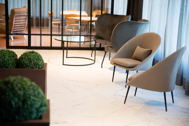 Interior de una sala con suelo de mármol blanco, varios sillones modernos de tela en tonos beige y gris, una mesa de cen