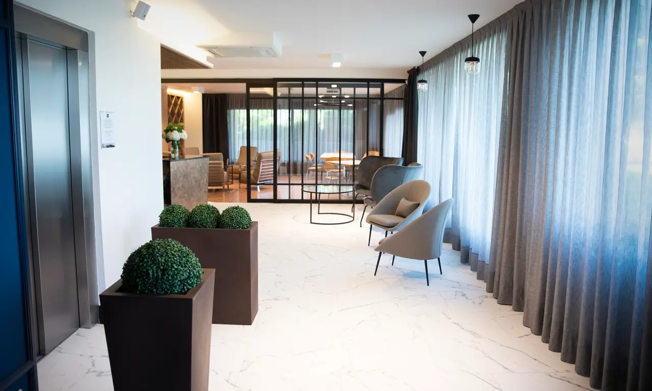 Interior de un amplio lobby o sala de hotel con suelo de mármol blanco, paredes blancas, ascensor a la izquierda