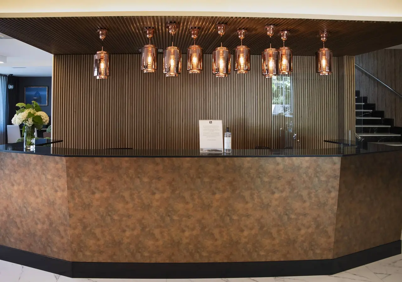 Mostrador de recepción de hotel con superficie curva en tonos marrones, pared trasera de madera vertical