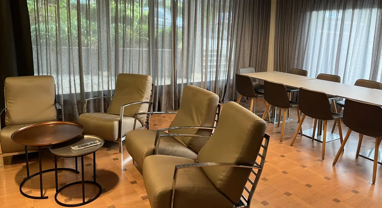 Interior de una sala con varias butacas de cuero beige con estructura metálica, mesas auxiliares redondas, una mesa