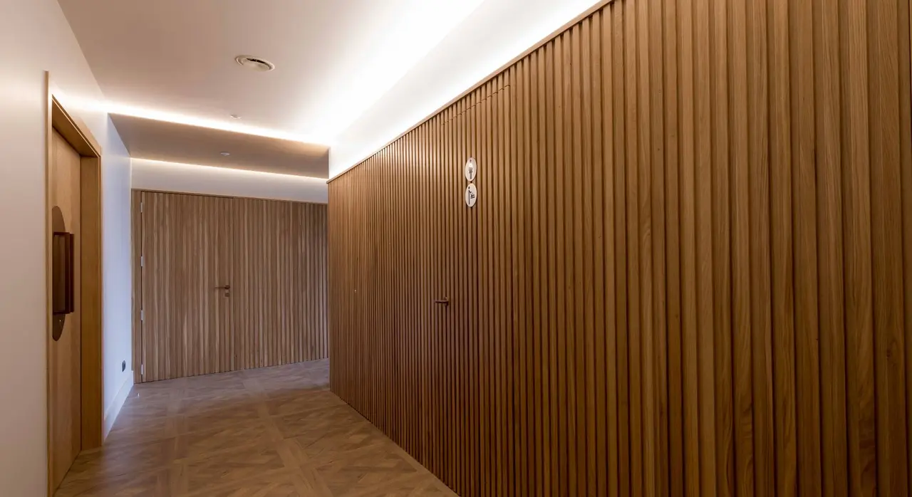 Pasillo interior de un alojamiento con suelo de madera en espiga, paredes y puertas revestidas en madera vertical