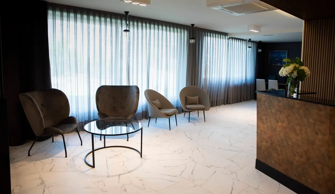 Interior de una sala de hotel con suelo de mármol blanco, cuatro sillones modernos alrededor de una mesa de centro