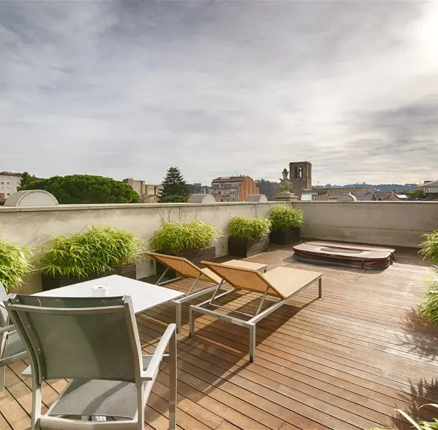 Terraza exterior con suelo de madera, dos tumbonas, mesa con sillas, macetas con plantas y jacuzzi privado circular