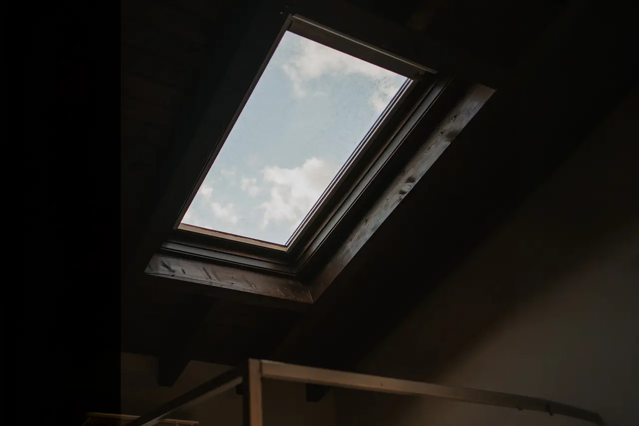 Vista hacia arriba de una claraboya rectangular en el techo de una habitación, con marco de madera oscura y cielo azul