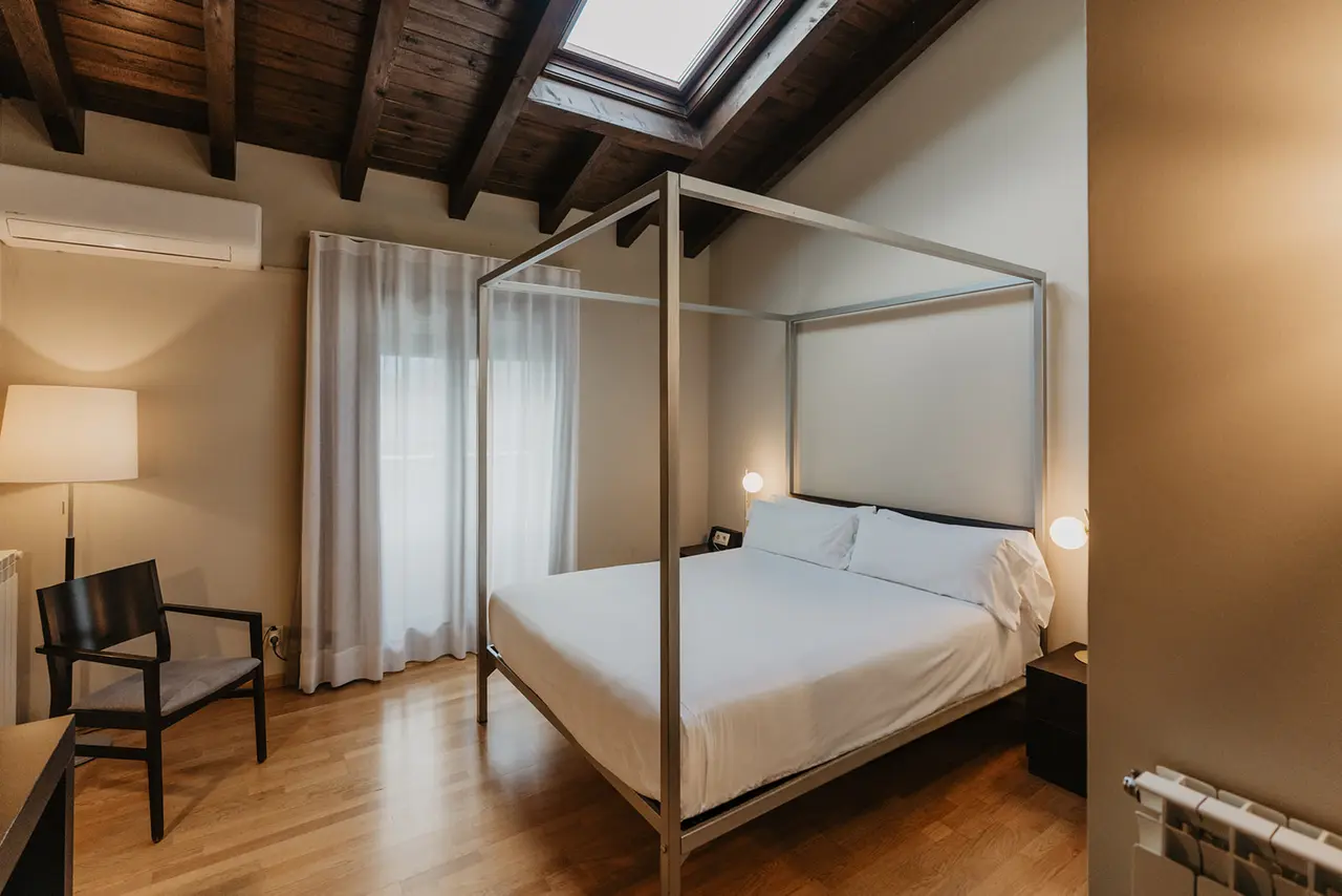 Habitación de hotel con cama de cuatro postes en el centro, suelo de madera, techo con vigas de madera oscura
