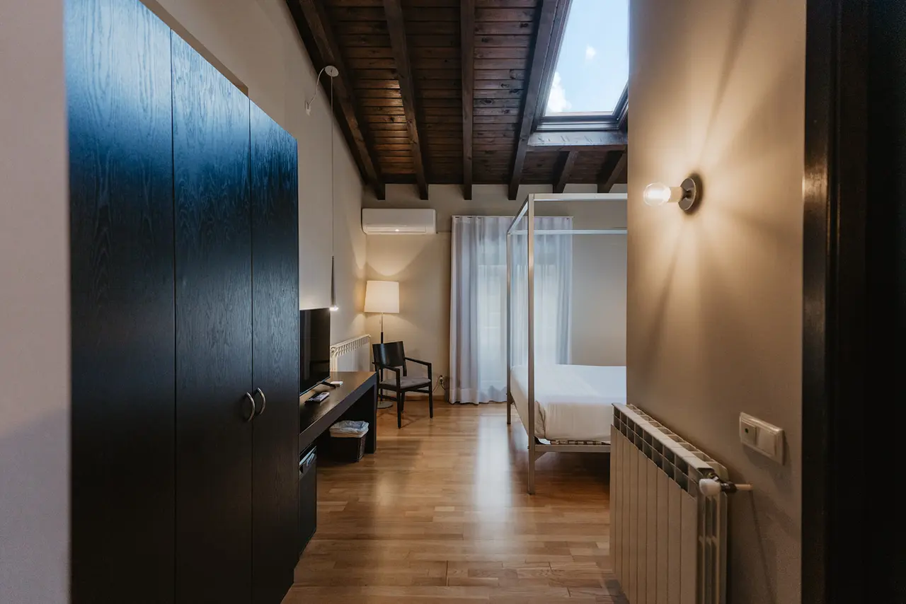 Vista de una habitación de hotel con cama de dosel, armario oscuro, escritorio con televisor, silla, techo de madera
