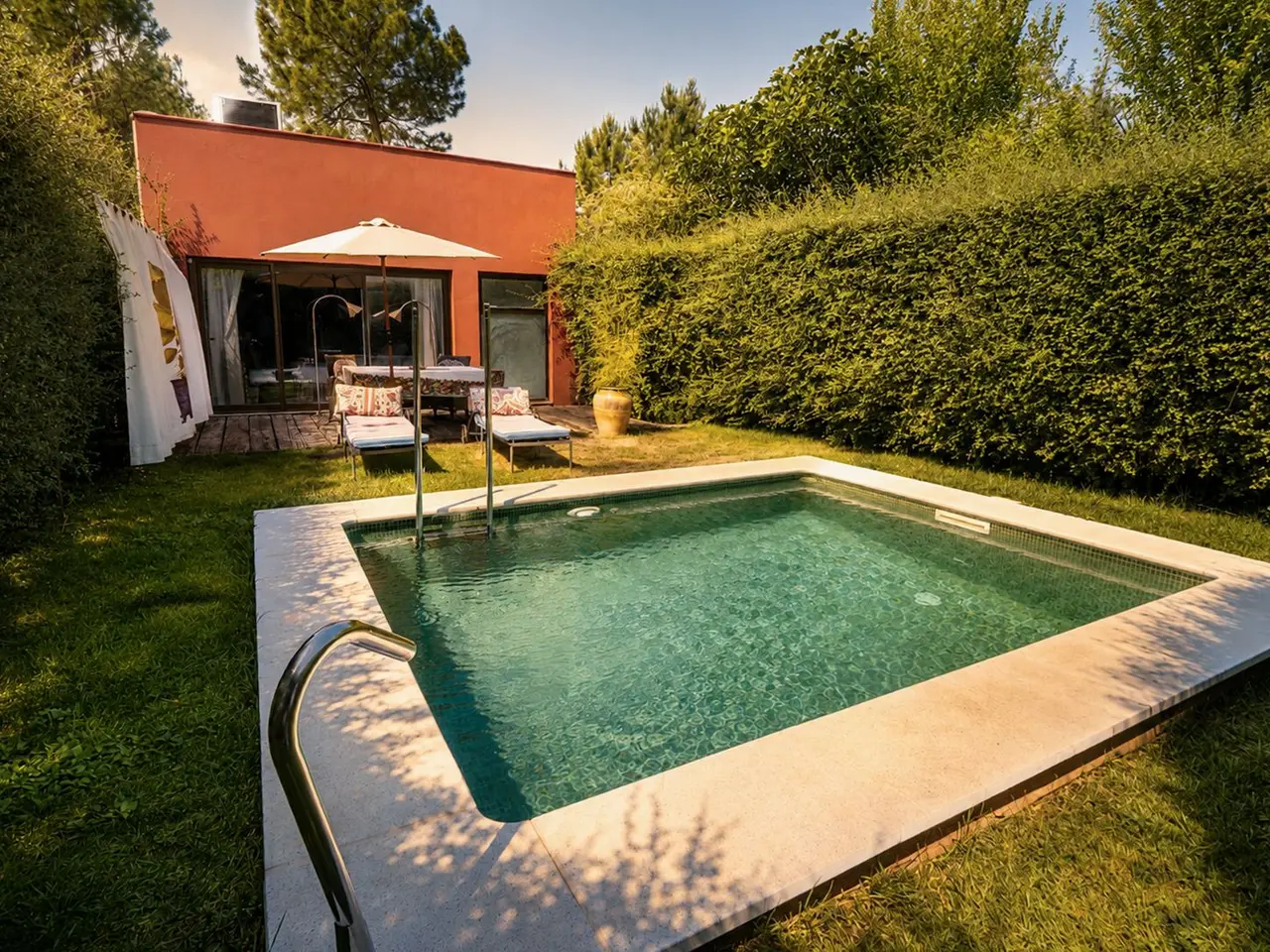 Piscina rectangular privada con agua clara, rodeada de césped, con escalera metálica y barandilla.