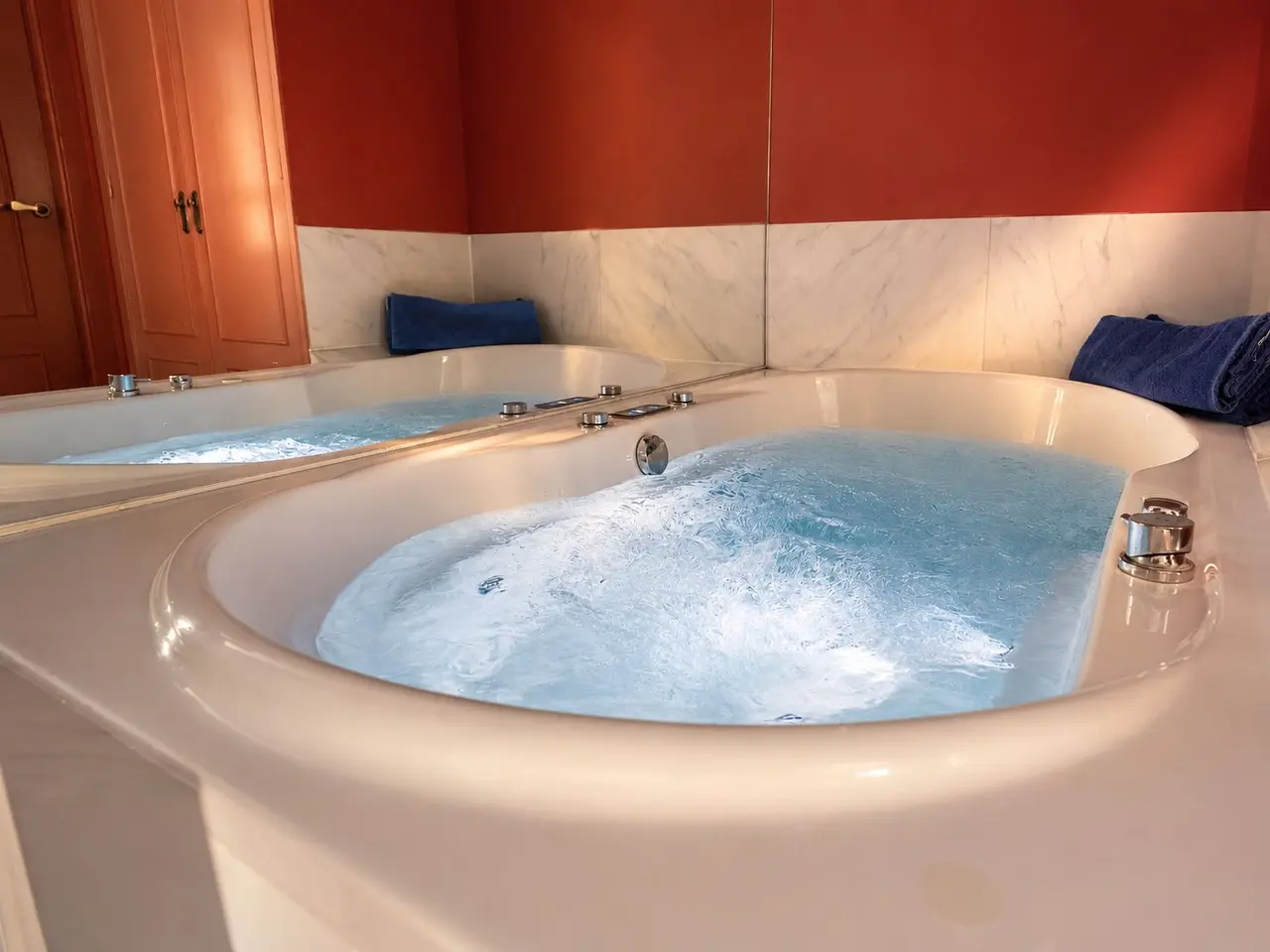Jacuzzi circular blanco con agua burbujeante en una habitación con paredes rojas y zócalo de mármol blanco.