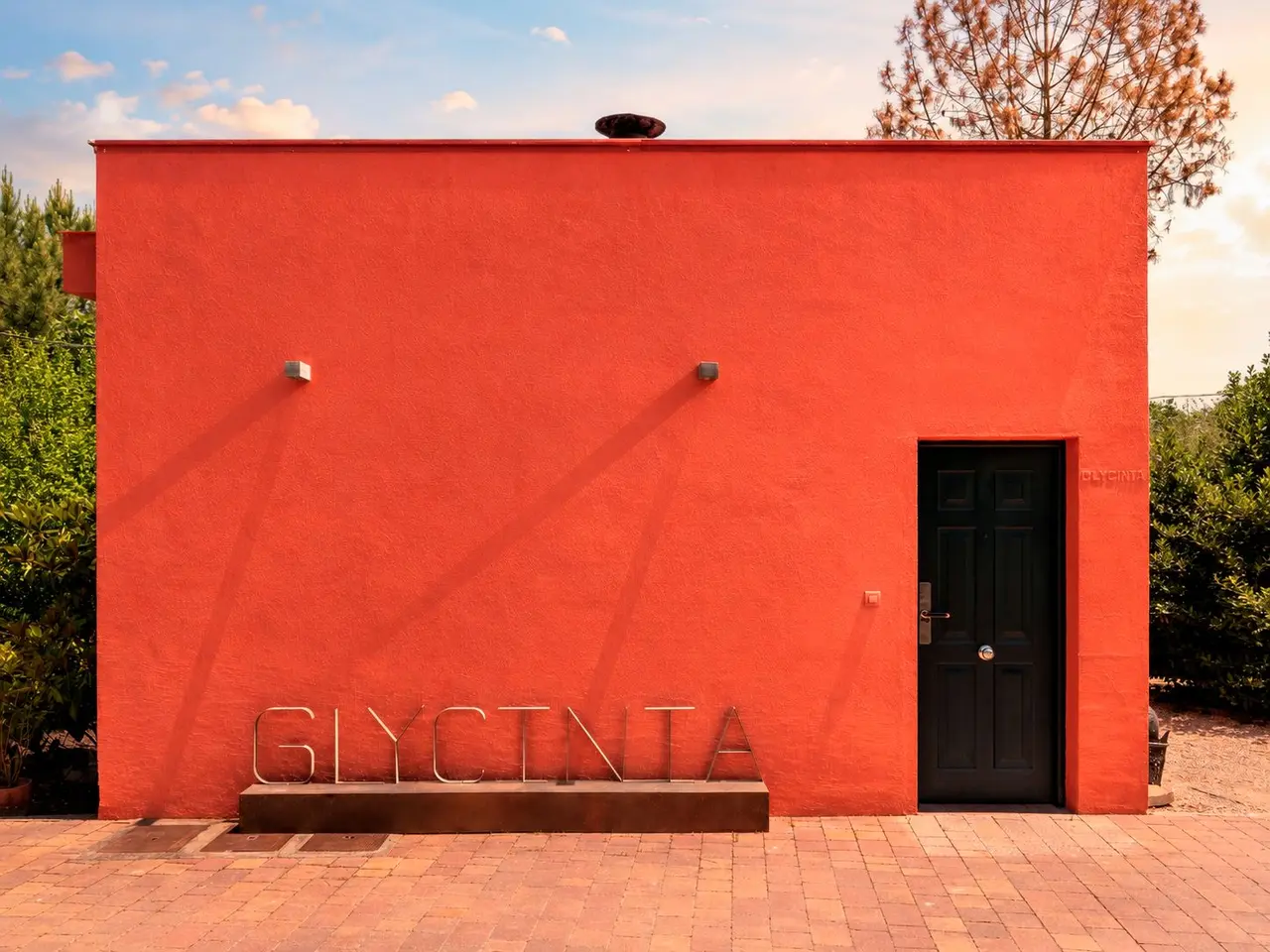 Fachada exterior de un edificio pintado de rojo intenso con una puerta negra, el nombre GLYCINIA en letras metálicas