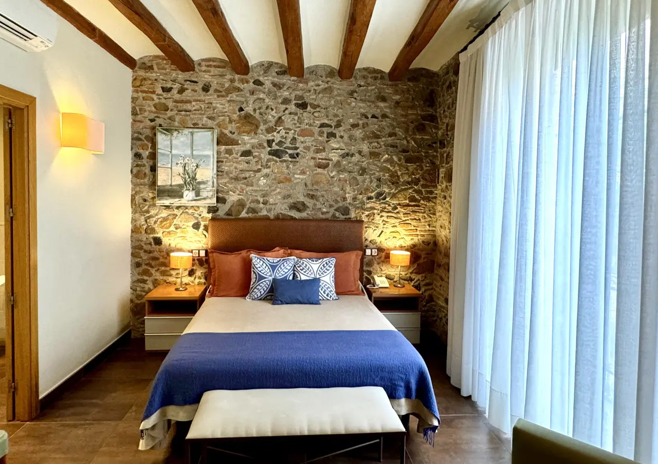 Habitación con cama doble, cabecero de cuero, colcha azul y cojines decorativos.