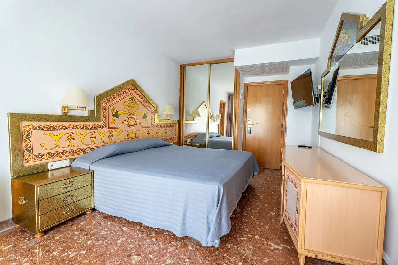 Vista de una suite de hotel con una cama doble, cabecero decorado con motivos egipcios en tonos dorados y terracota