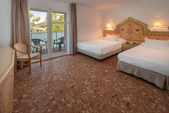 Vista de una suite de hotel con dos camas individuales, suelo de terrazo rojizo, cabeceros decorados con motivos