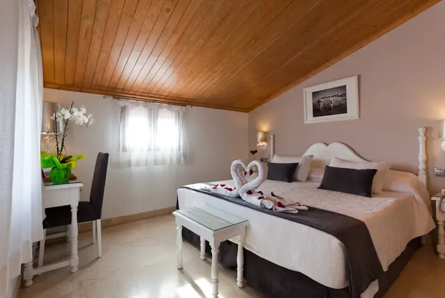 Habitación doble con cama grande vestida en tonos blancos y grises, toallas decorativas en forma de cisnes