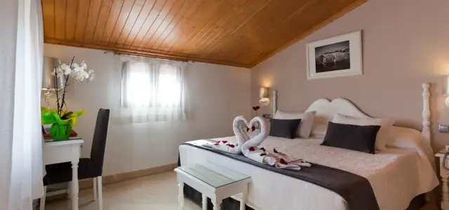 Habitación doble con cama grande vestida en tonos beige y grises, decorada con toallas en forma de cisnes y pétalos